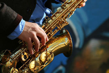 Obraz premium Young man with saxophone outside near the old painted wall