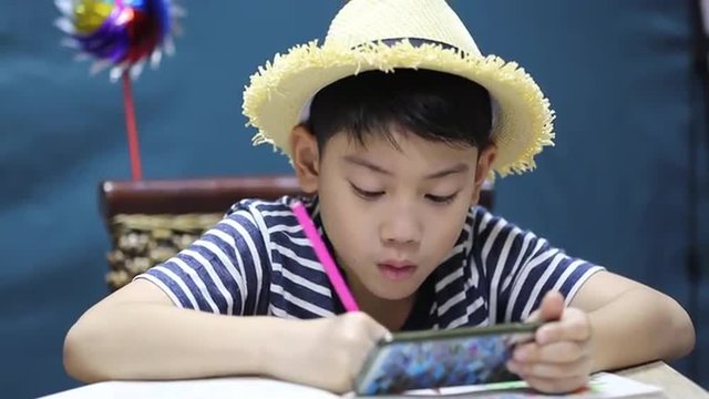 little asian happy boy looking on screen of cell phone and painting, with smile face