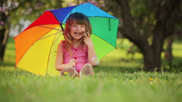 Cute girl with umbrella sitting on grass and laughing