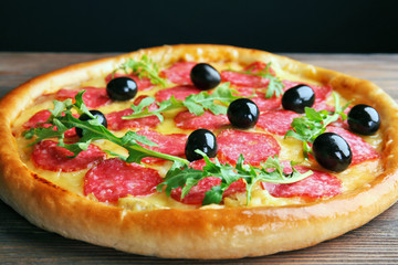 Tasty pizza with salami and olives on wooden table against black background