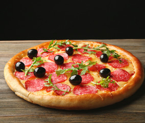 Tasty pizza with salami and olives on wooden table against black background