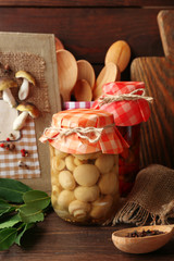 Jars with pickled vegetables, beans, spices and kitchenware on wooden background