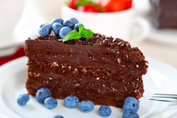 Chocolate cake with chocolate cream and fresh berries on plate, on wooden table, on light background