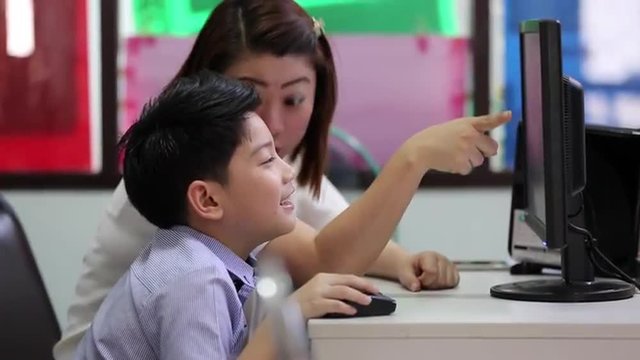 Asian child looking at the computer in library with their teacher in elementary school