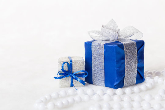 Blue Christmas gift box with shiny silver ribbon and beads on white background. Copyspace for your greeting or wishes