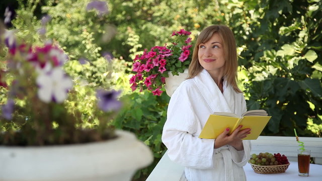 Young adult in a bathrobe on the front porch. Girl reading a book and smiling at the camera. Zoom