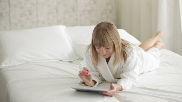 Young woman lying on bed and using touchpad