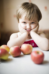 Fototapeta na wymiar Маленькая девочка сидит за столом с яблоками