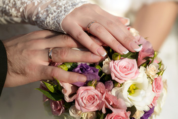 Obraz na płótnie Canvas Hands of the groom and the bride with wedding rings and a wedding bouquet from roses