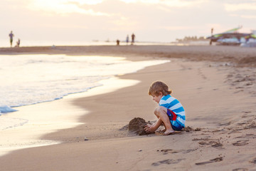 Happy little kid boy having fun with sand castle by ocean
