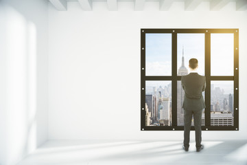 Fototapeta premium Businessman in white empty loft room with megapolis city view