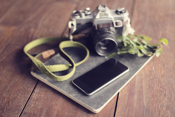 Vintage camera, blank smartphone, diary and leaves on wooden tab