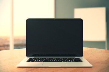 Blank black laptop screen on wooden table at empty office backgr