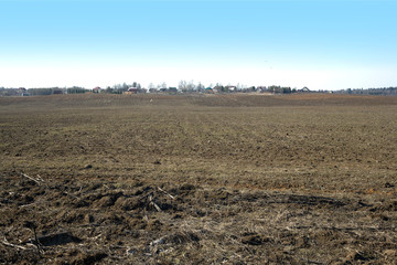 Fototapeta premium Country landscape with plowed field and a village far away on spring day
