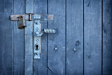 Old vintage door handle with a rusty padlock on a stunning blue colored wood door