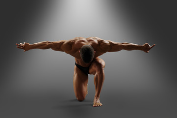muscular male model stands on one knee, arms outstretched to the side and looks down