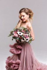 Beautiful woman with a bouquet in a long pink dress.