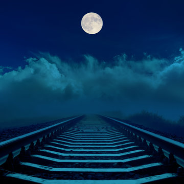 full moon in dark sky over railroad and clouds