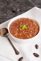 Chocolate porridge with banana in white bowl, decorated mint
