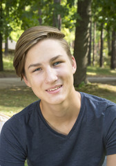 Smiling boy is sitting on green grass in nature.