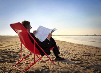 Businessman reading the newspaper at the seaside