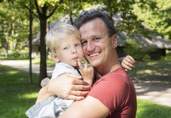 Happy dad holding his son, little funny kid boy on arm sunny day