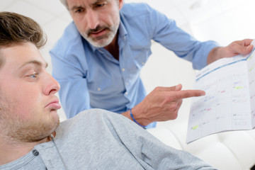 Man pointing angrily at book, young man feigning ignorance