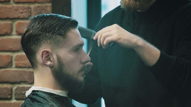Barber cuts the hair of the client with scissors