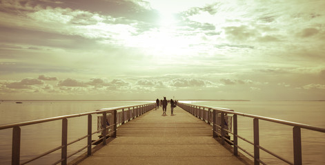Fototapeta premium Long pier over the sea shore with sihouette of walkers
