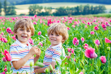 Two happy little blond children in blooming poppy field