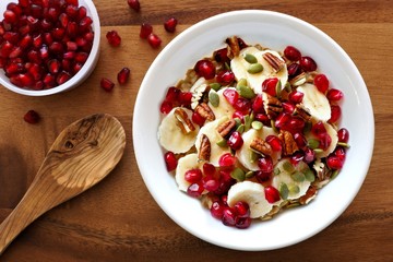 Healthy breakfast oatmeal with pomegranate, bananas, seeds and nuts, overhead scene on wood