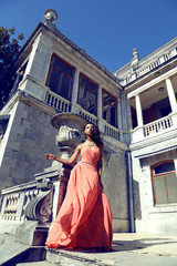 girl wears elegant coral dress with bijou ,posing beside antic palace