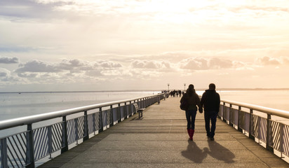 Silhouette of a couple holding hands, walking on the pier, to the sea, evening light leak sunset