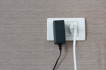 White and black cable plugged in a white electric outlet mounted