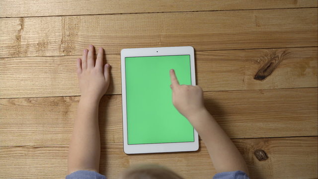 Little cute baby girl sitting on a wooden table uses a Tablet PC, touches finger the screen of touchpad