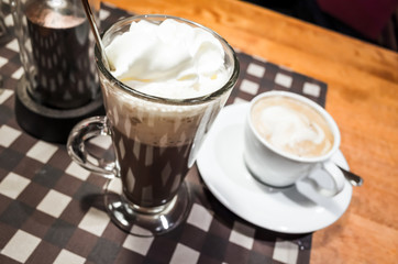 Glass of hot chocolate and white cup of cappuccino