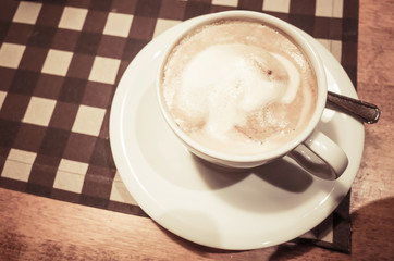 White cup of cappuccino stands on wooden table
