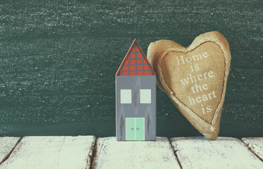 image of vintage wooden colorful house and fabric heart on wooden table in front of  blackboard. faded retro filtered image