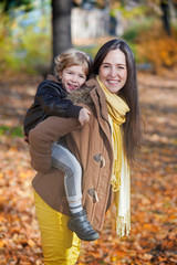 Fototapeta premium Happy mother piggybacking her son in autumn.