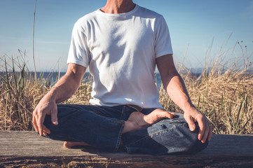 Man sits in yoga pose, outside in the sunshine.