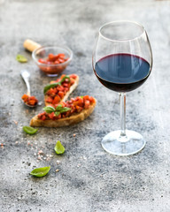 Wine appetizer set. Glass of red wine, brushettas with fresh tomato and basil on over rustic grunge grey surface
