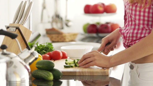 Young woman in kitchen cutting vegetables on cutting board