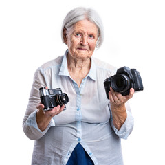 Senior woman holding old analogue and modern digital cameras in hands, choice concept