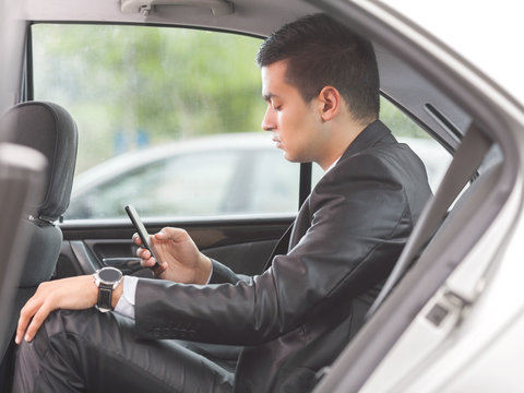 Young businessman using mobile phone while sitting on the back seat of the car