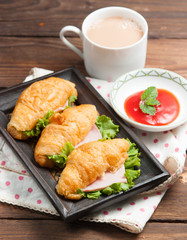 Fresh croissant ham and salad leaf with sauce on dark wooden bac