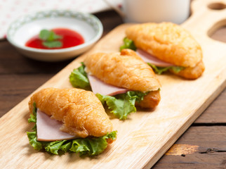 Fresh croissant ham and salad leaf with sauce on dark wooden bac