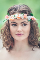 Closeup portrait of beautiful white Caucasian girl with hazel eyes, long wavy curly hair and flowers chaplet on head. Attractive young woman model in park outside, country village hippie style