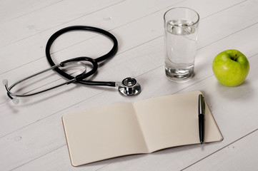 Open notebook with pen, stethoscope, apple and a glass water