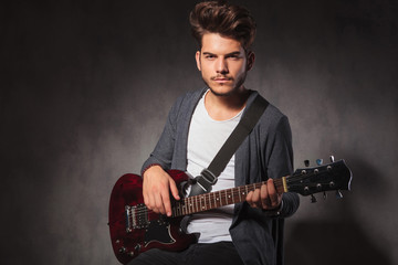 fashionable artist playing guitar in dark studio background