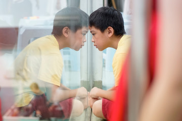 Sad upset waiting boring depressed child (boy) near a window, reflection.